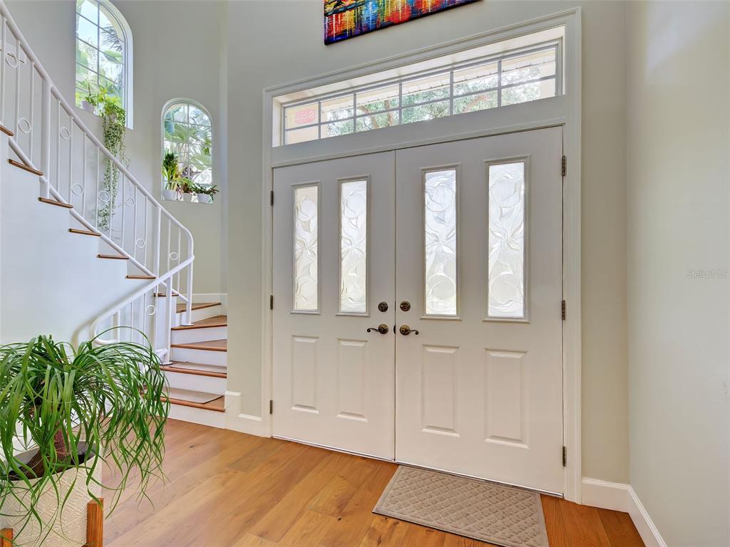 A bright entryway features double front doors, a curved staircase, and light wood flooring — 5026 HANGING MOSS LANE, SARASOTA, FL