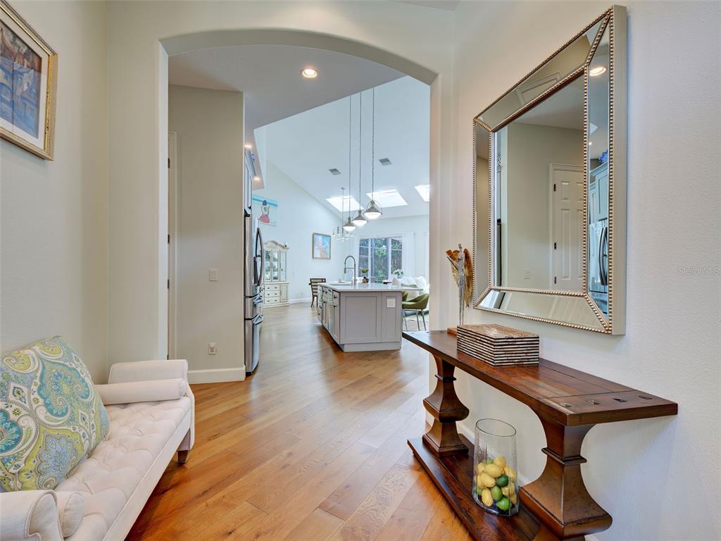 A hallway with a bench and console table leads into a kitchen with vaulted ceilings — 5026 HANGING MOSS LANE, SARASOTA, FL