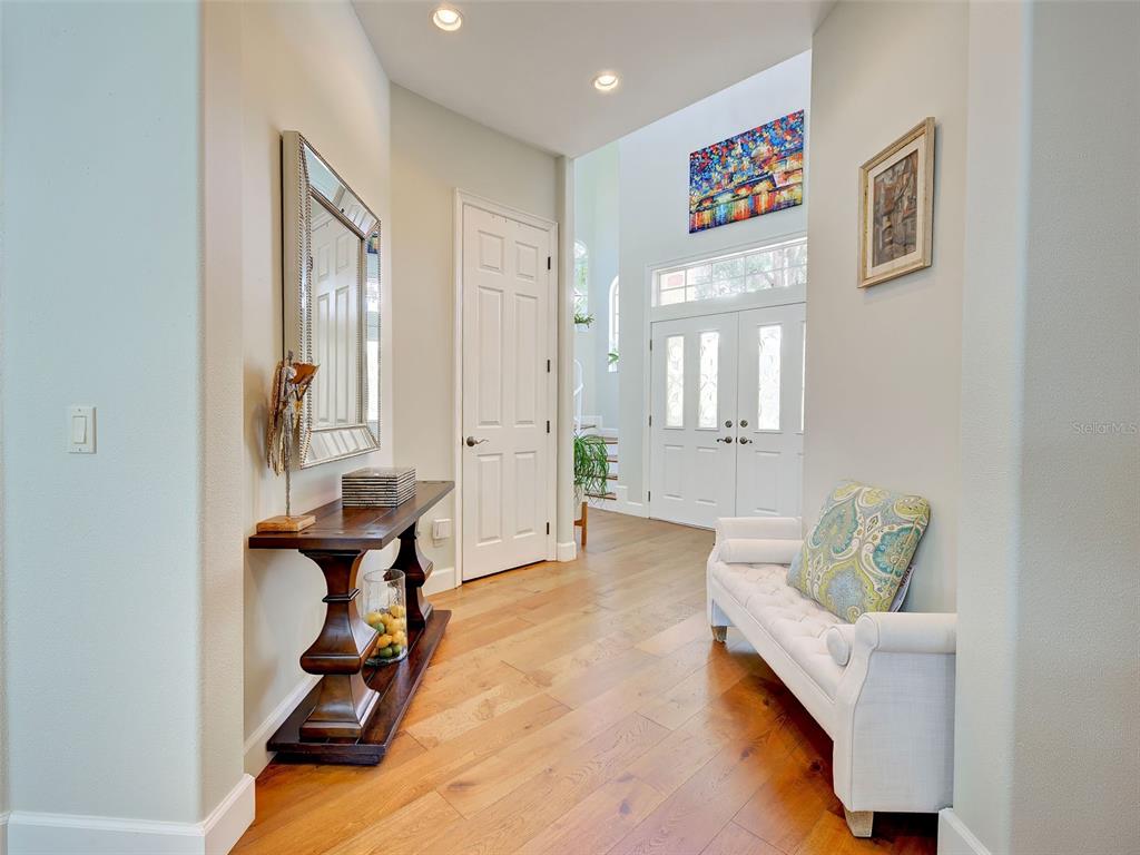 A bright entryway features hardwood floors, a white bench, a console table, and double doors — 5026 HANGING MOSS LANE, SARASOTA, FL
