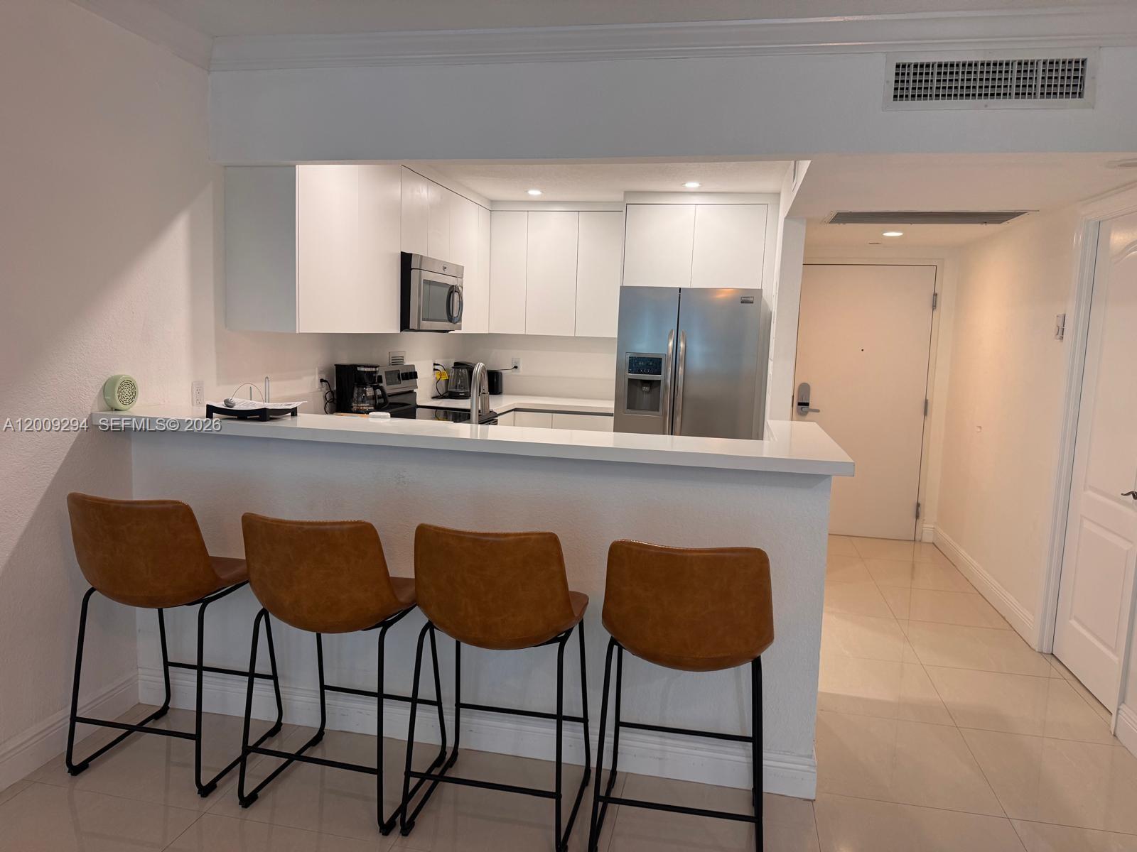 A kitchen features white cabinets, stainless steel appliances, and a breakfast bar with four stools — 2301 Collins Ave # 427, Miami Beach FL 33139, MIAMI BEACH, FL
