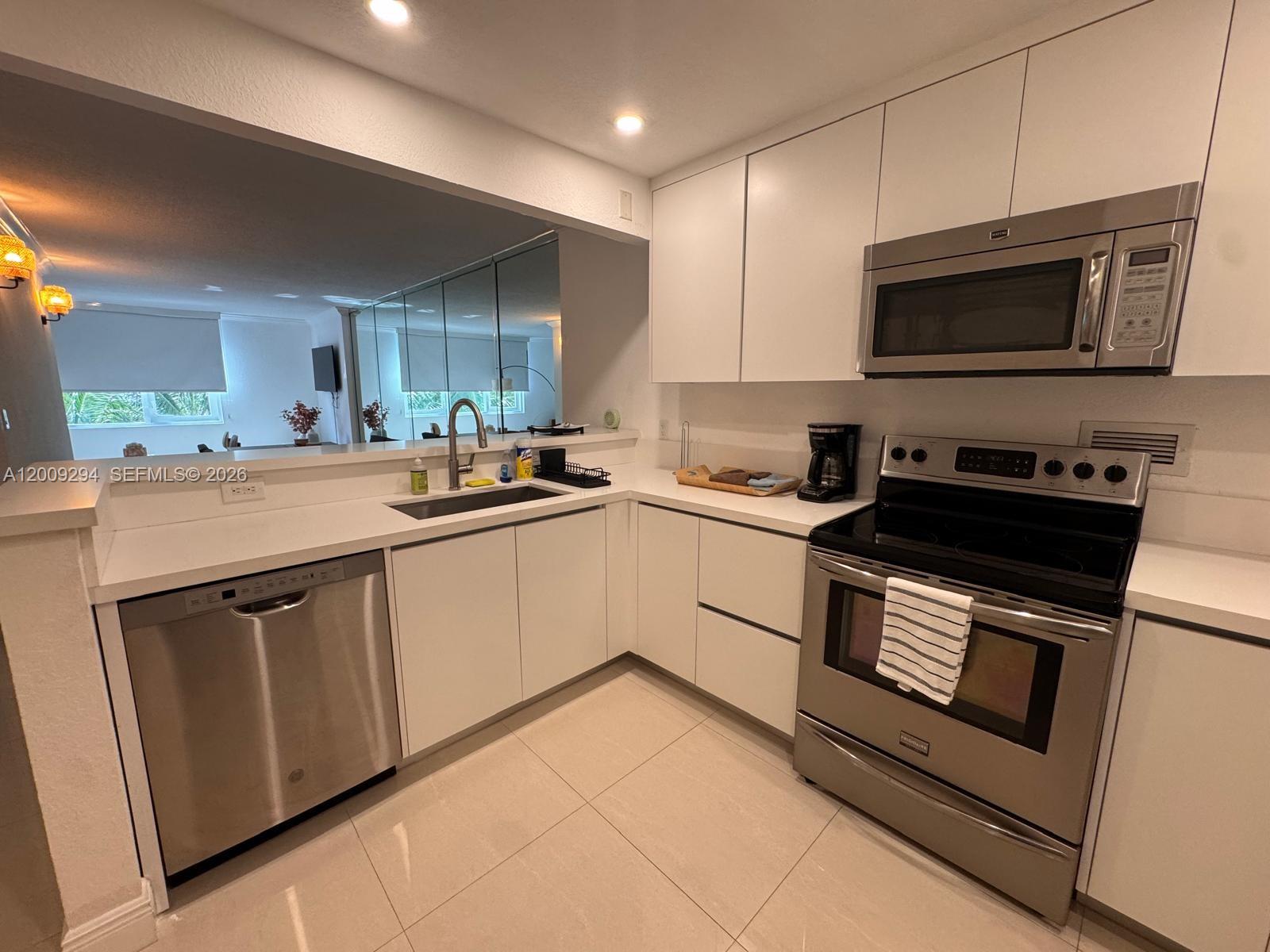 A modern kitchen features white cabinets, stainless steel appliances, and a pass-through window — 2301 Collins Ave # 427, Miami Beach FL 33139, MIAMI BEACH, FL