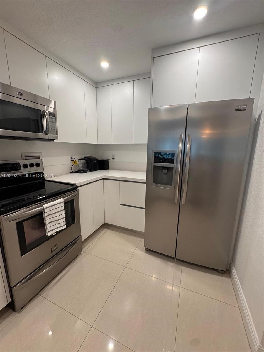 A modern kitchen features white flat-panel cabinets, stainless steel appliances, and light-colored tile flooring — 2301 Collins Ave # 427, Miami Beach FL 33139, MIAMI BEACH, FL