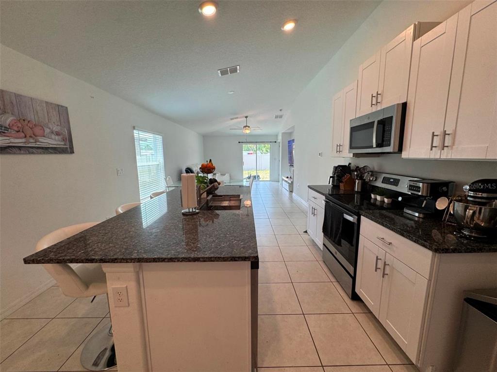 A kitchen with white cabinets, granite countertops, and a large island overlooks an open living area — 2034 OLD PASTURE LANE, LAKELAND, FL