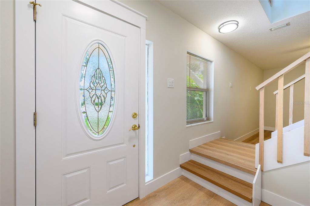 An entryway features a white door with a glass insert, wood-look flooring, and wooden stairs — 1612 1ST ST, INDIAN ROCKS BEACH, FL