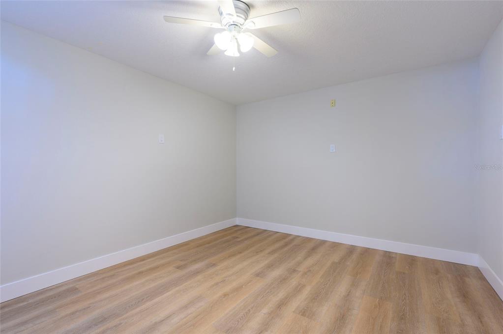An empty room features light-colored walls, wood-look flooring, and a ceiling fan — 1612 1ST ST, INDIAN ROCKS BEACH, FL
