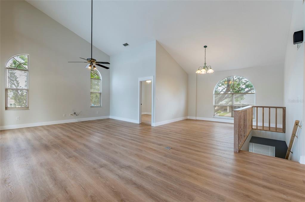 A spacious living room features vaulted ceilings, light wood-look flooring, and a staircase with railings — 1612 1ST ST, INDIAN ROCKS BEACH, FL