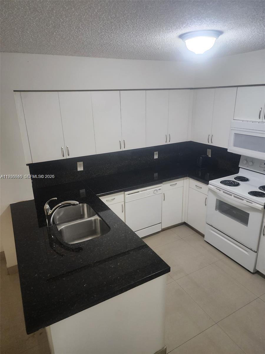 A kitchen features white cabinets, black countertops, and white appliances — 4560 NW 107th Ave # 12, Doral FL 33178, DORAL, FL