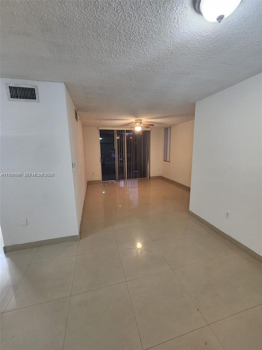 An empty living room features light-colored tile flooring, white walls, and a sliding glass door — 4560 NW 107th Ave # 12, Doral FL 33178, DORAL, FL