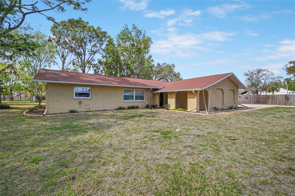 A single-story house with a tan stucco exterior and a red shingled roof — 3065 KNOX MC RAE DRIVE, TITUSVILLE, FL