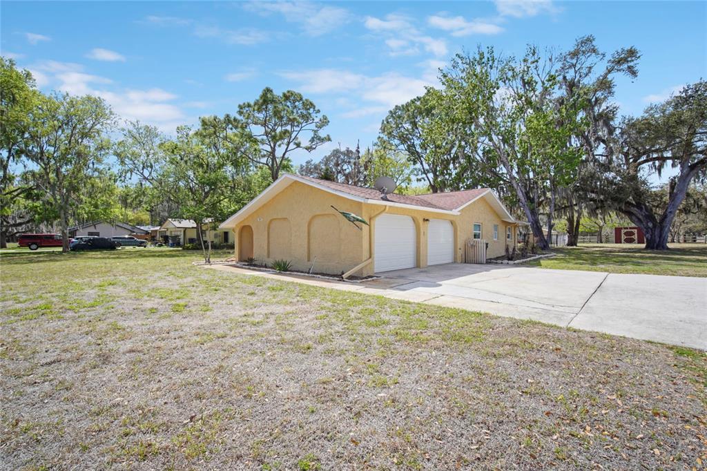 A yellow house with a two-car garage sits on a large, grassy lot with trees — 3065 KNOX MC RAE DRIVE, TITUSVILLE, FL