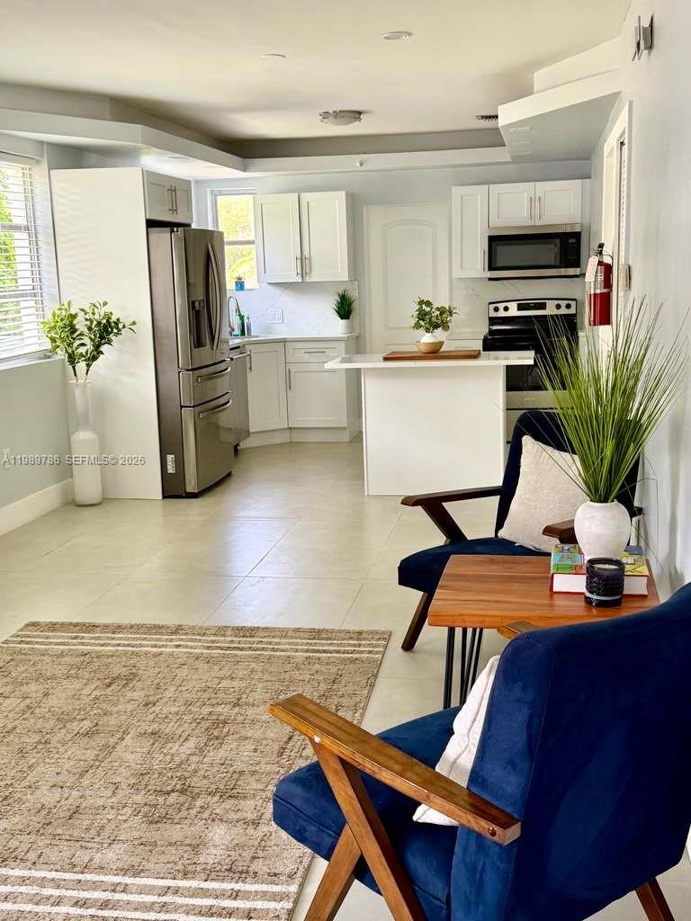 A kitchen with white cabinetry, stainless steel appliances, and an island opens to a living area — 715 Hollywood Blvd, Hollywood FL 33019, HOLLYWOOD, FL