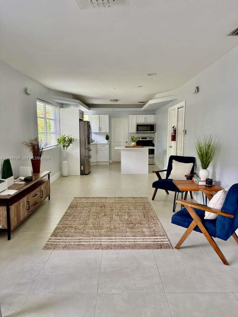 An open-concept living room and kitchen featuring white cabinetry, tile flooring, and blue accent chairs — 715 Hollywood Blvd, Hollywood FL 33019, HOLLYWOOD, FL
