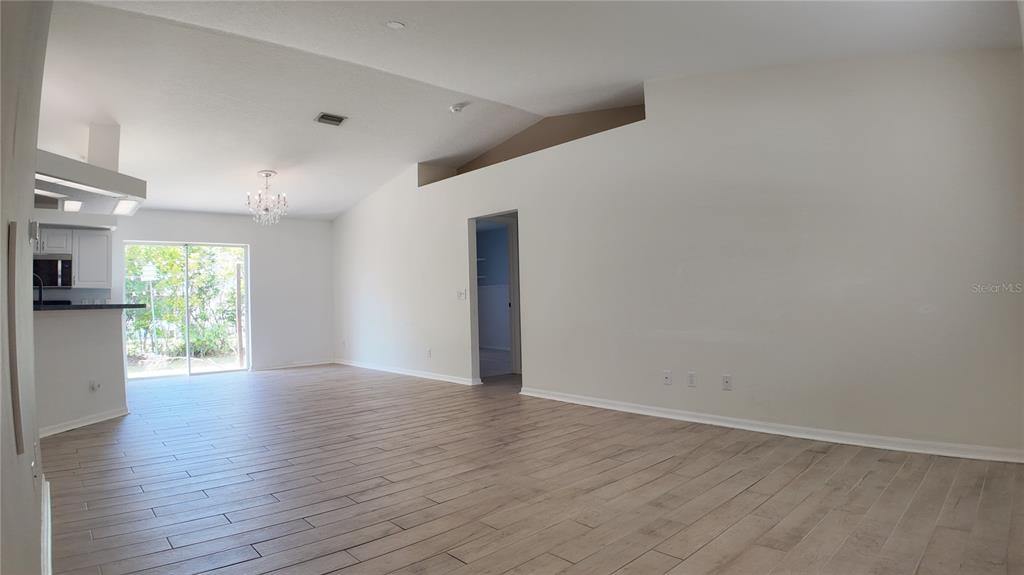 An open-concept living area features vaulted ceilings, light wood-look tile flooring, and a sliding door — 4915 BARCELONA AVENUE, SARASOTA, FL