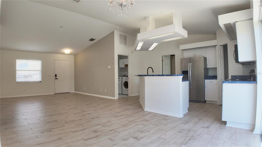 An open-concept kitchen and living area featuring white cabinetry, blue countertops, and light wood-look flooring — 4915 BARCELONA AVENUE, SARASOTA, FL