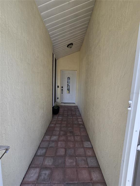 A narrow outdoor entryway features a tiled floor, stucco walls, and a white front door — 7264 LINDHURST STREET, SPRING HILL, FL