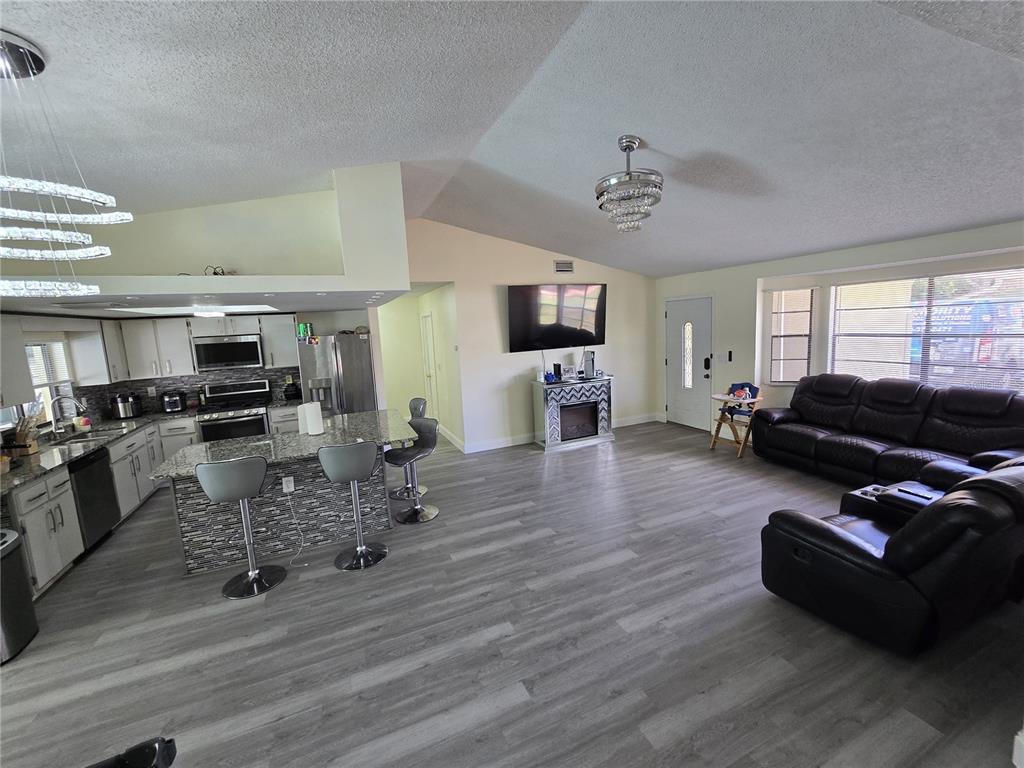 An open-concept kitchen and living area features gray wood-look flooring and a granite island — 7264 LINDHURST STREET, SPRING HILL, FL