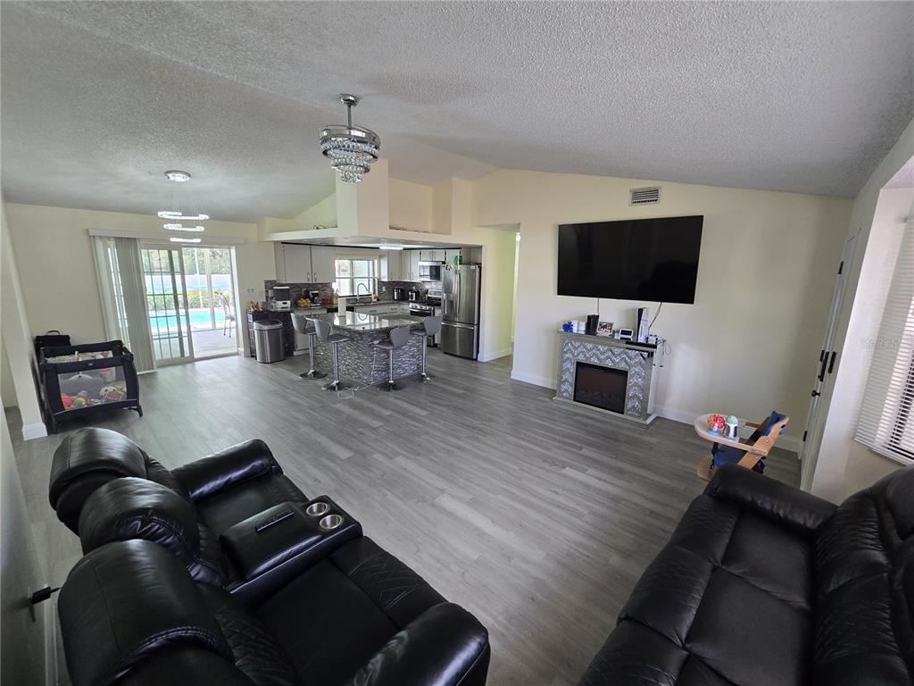 An open-concept living room and kitchen featuring gray wood-look flooring and a stone fireplace — 7264 LINDHURST STREET, SPRING HILL, FL