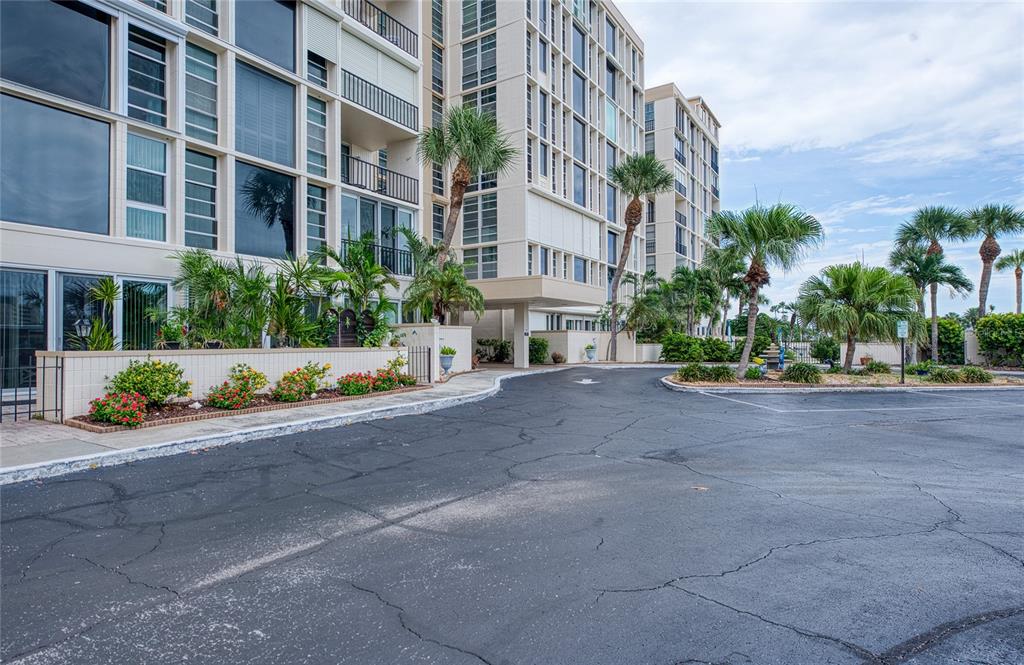 A multi-story apartment building features a paved driveway, palm trees, and a landscaped flower bed — 7400 SUN ISLAND DRIVE S UNIT 709, SOUTH PASADENA, FL