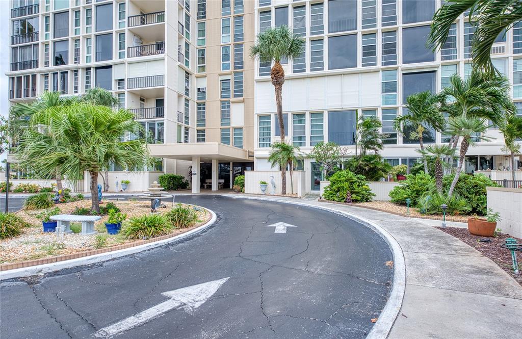 A paved driveway leads to the entrance of a multi-story residential building with palm trees — 7400 SUN ISLAND DRIVE S UNIT 709, SOUTH PASADENA, FL