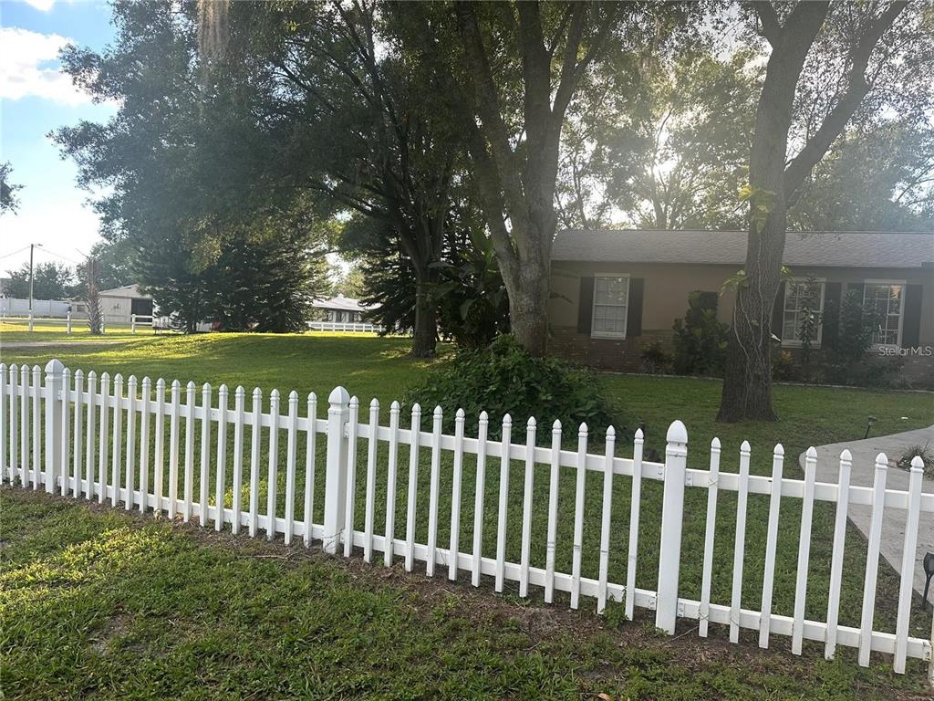 A white picket fence encloses a grassy front yard with trees and a single-story house — 10520 HENDERSON ROAD, TAMPA, FL