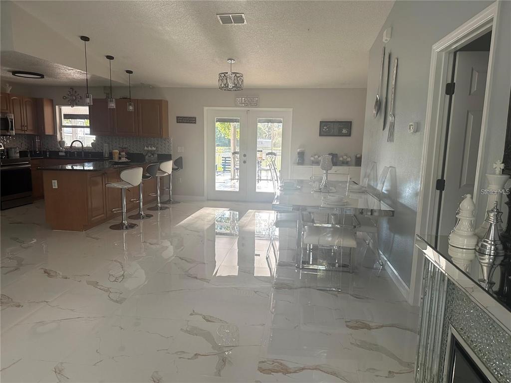 An open-concept kitchen and dining area features white marble-look tile flooring and wooden cabinetry — 10520 HENDERSON ROAD, TAMPA, FL