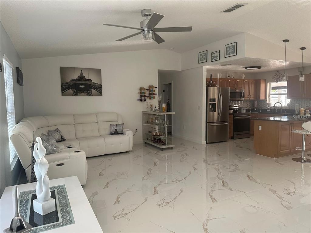 An open-concept living room and kitchen featuring white marble-look tile flooring and a white sofa — 10520 HENDERSON ROAD, TAMPA, FL