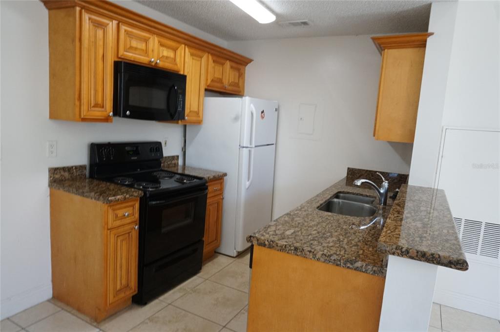 A kitchen features honey-oak cabinets, granite countertops, black appliances, and light-colored tile flooring — 2584 GRASSY POINT DRIVE UNIT 204, LAKE MARY, FL