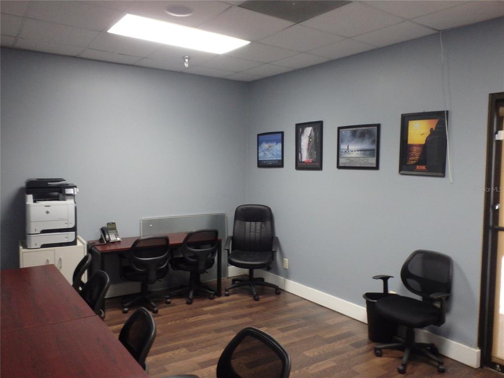 An office room features a dark wood desk, several rolling chairs, and framed wall art — 4984 PALM COAST PARKWAY NW UNIT 7, PALM COAST, FL