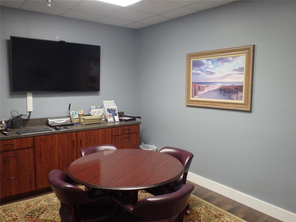 A small office features a round table, four chairs, a television, and wooden cabinetry — 4984 PALM COAST PARKWAY NW UNIT 7, PALM COAST, FL