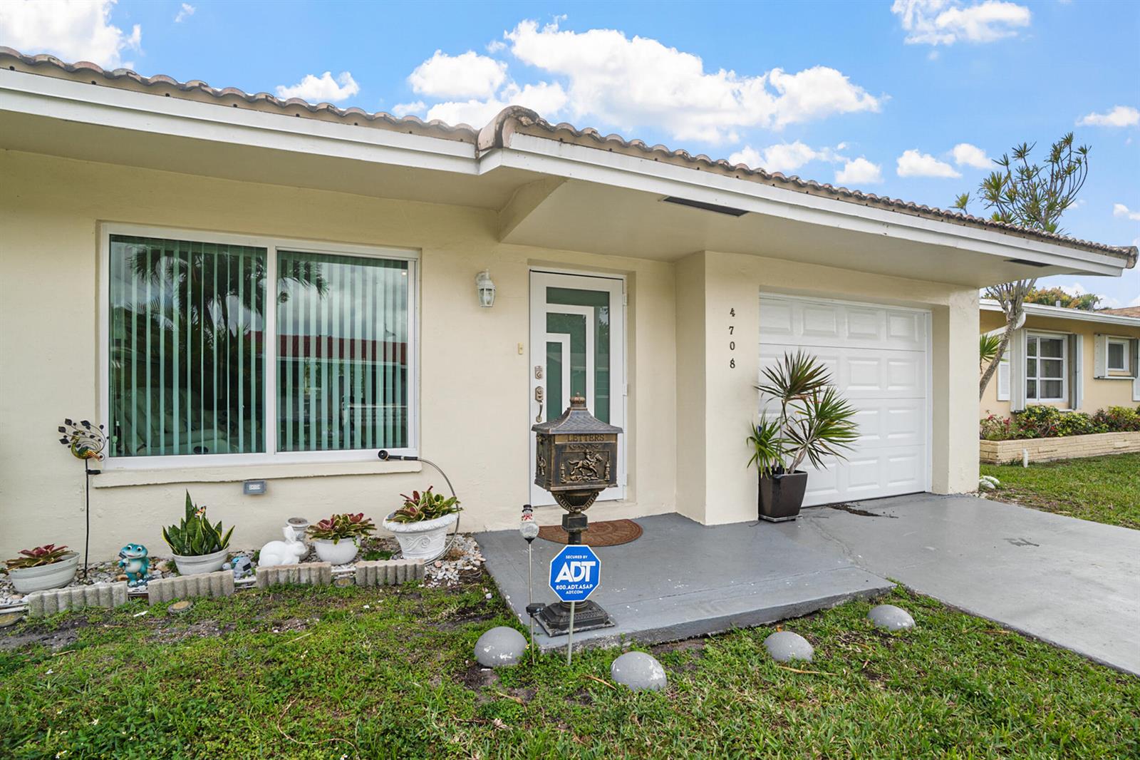 The exterior of a single-story house features a white garage door and a front entrance — 4708 NW 49th Drive, Tamarac FL 33319, TAMARAC, FL