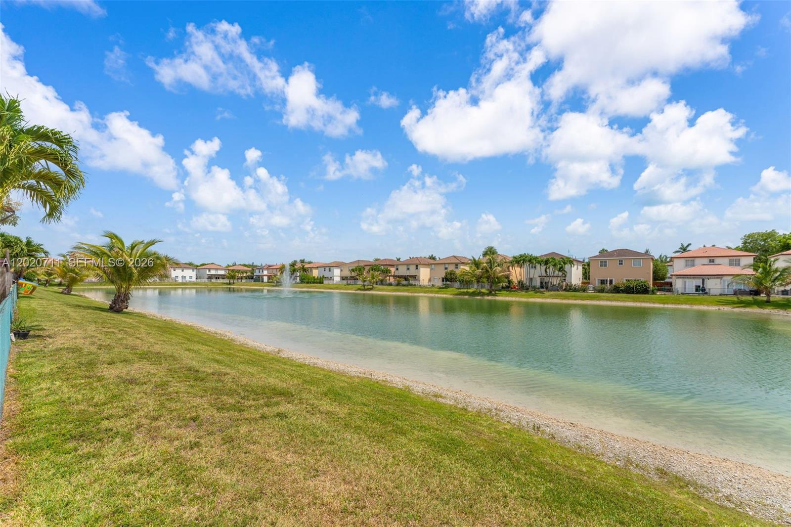 A grassy bank overlooks a lake with a fountain and houses in the background — 11318 NW 44th Ter, Doral FL 33178, DORAL, FL