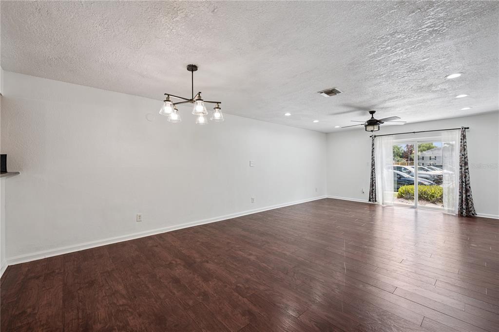 A spacious living room features dark wood-look flooring, a chandelier, and a sliding glass door — 193 LEWFIELD CIRCLE, WINTER PARK, FL