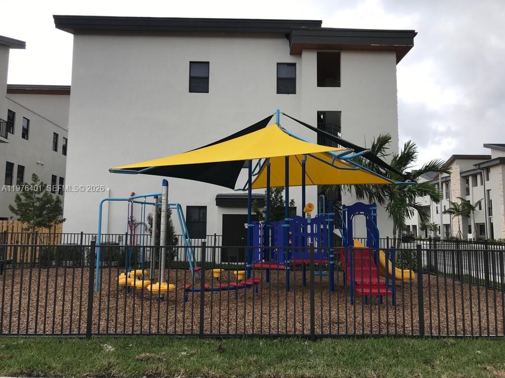 A fenced playground with a yellow shade sail sits in front of a modern apartment building — 10431 NW 82nd St # 5, Doral FL 33178, DORAL, FL