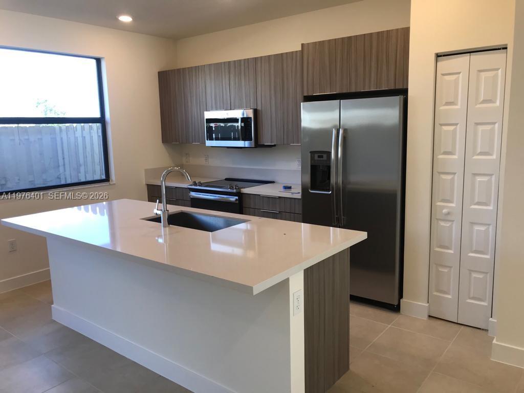 A modern kitchen features a white island, stainless steel appliances, and wood-toned cabinetry — 10431 NW 82nd St # 5, Doral FL 33178, DORAL, FL