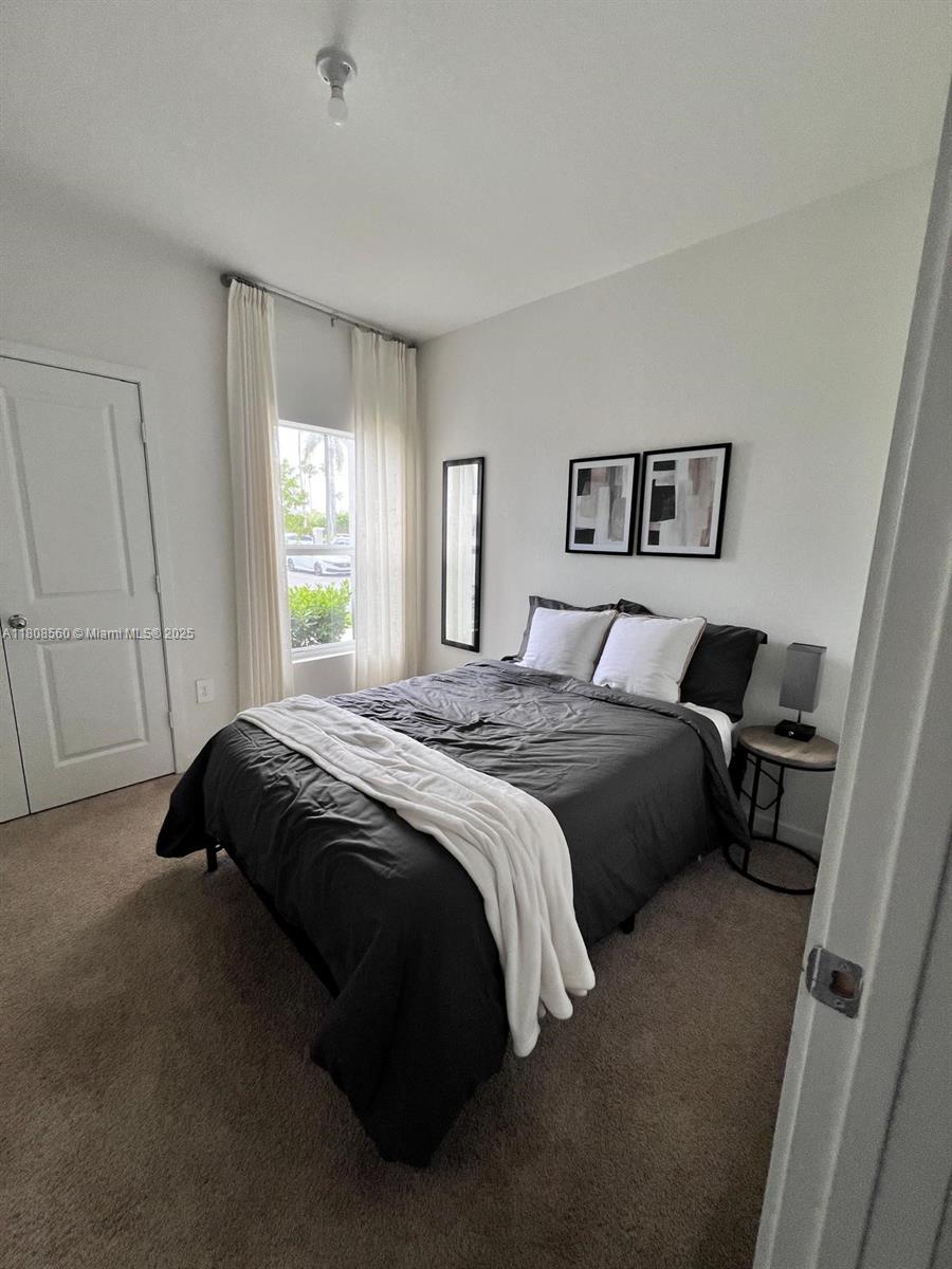 A bedroom features a bed with dark bedding, white pillows, and a window with curtains — 245 NE 3rd Ct, Florida City FL 33034, FLORIDA CITY, FL