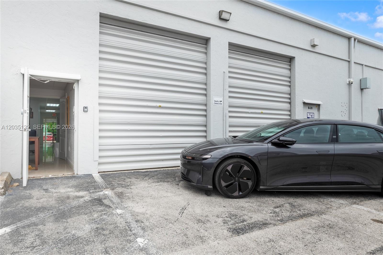 A dark sedan is parked in front of a white building with two roll-up doors — 16155 SW 117th Ave # B21, Miami FL 33177, MIAMI, FL