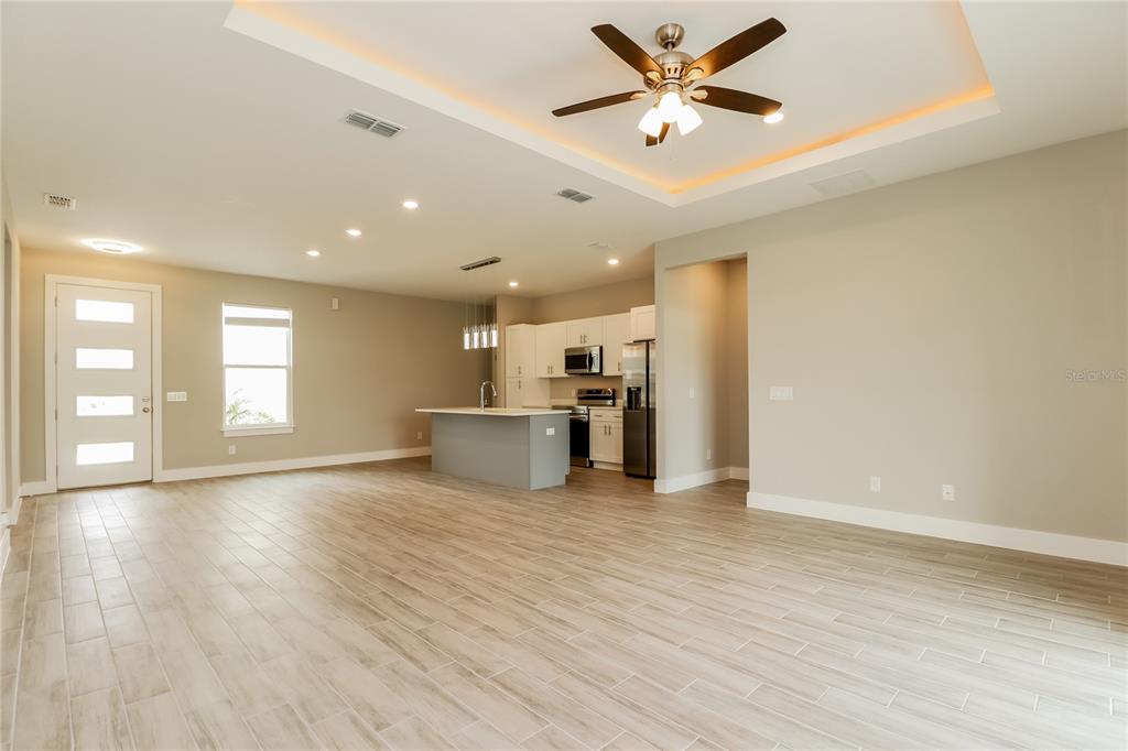 An open-concept living area features a kitchen with an island and light wood-look flooring — 260 GLADIOLA COURT, KISSIMMEE, FL