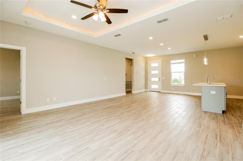 An open-concept living area features light wood-look tile flooring, a tray ceiling, and a kitchen — 260 GLADIOLA COURT, KISSIMMEE, FL