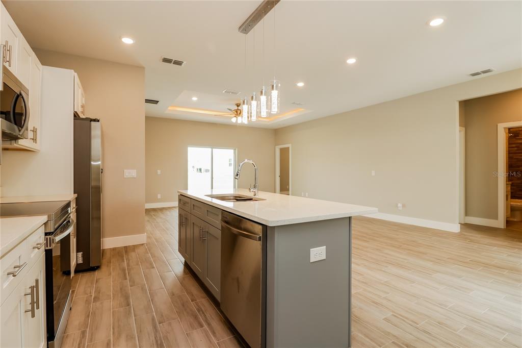 A modern kitchen features a gray island with a sink, stainless appliances, and tile flooring — 260 GLADIOLA COURT, KISSIMMEE, FL