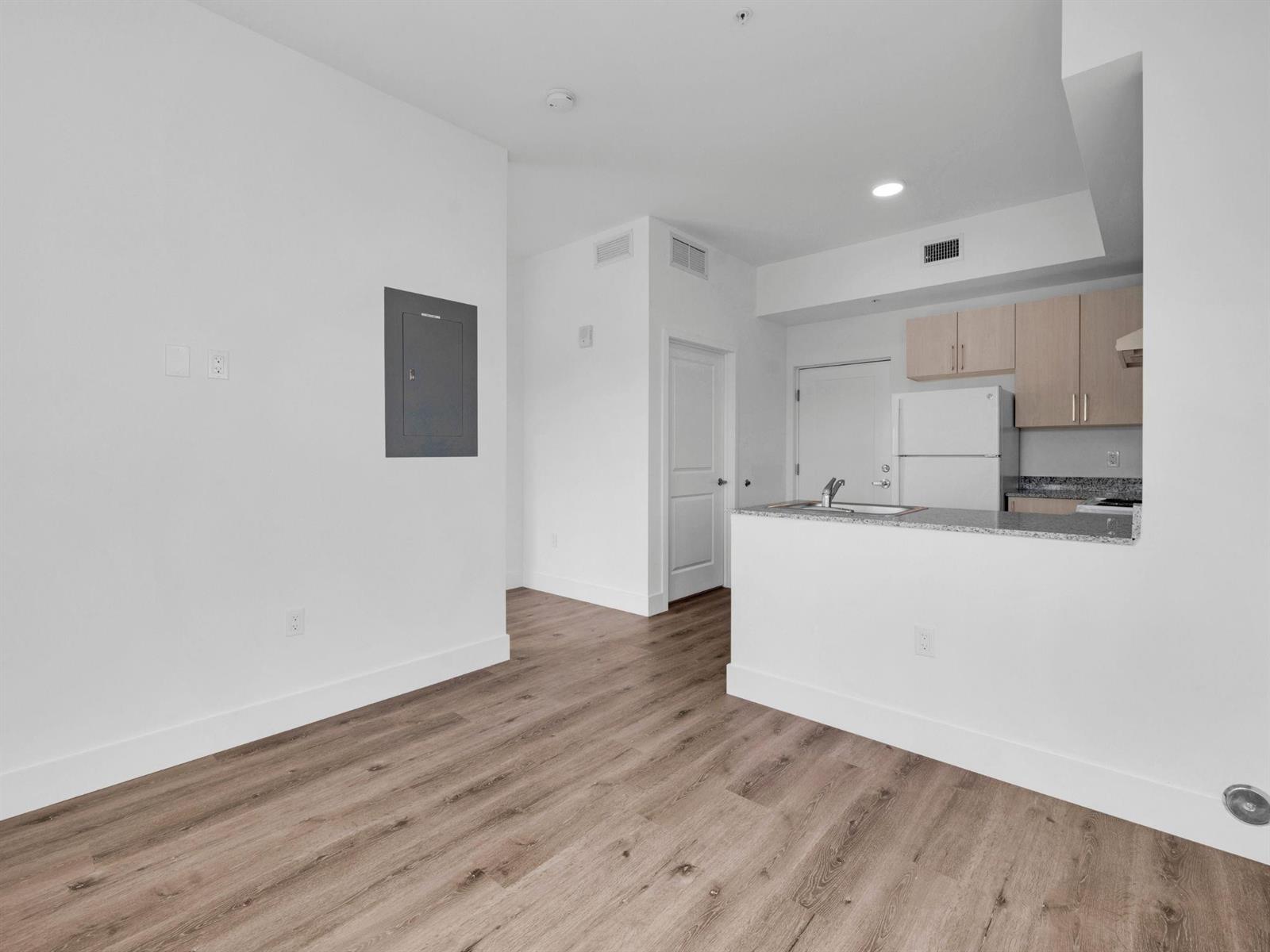 A living area with wood-look flooring leads to an open kitchen with light-colored cabinets — 2130 NW 37th Street, Miami FL 33142, MIAMI, FL