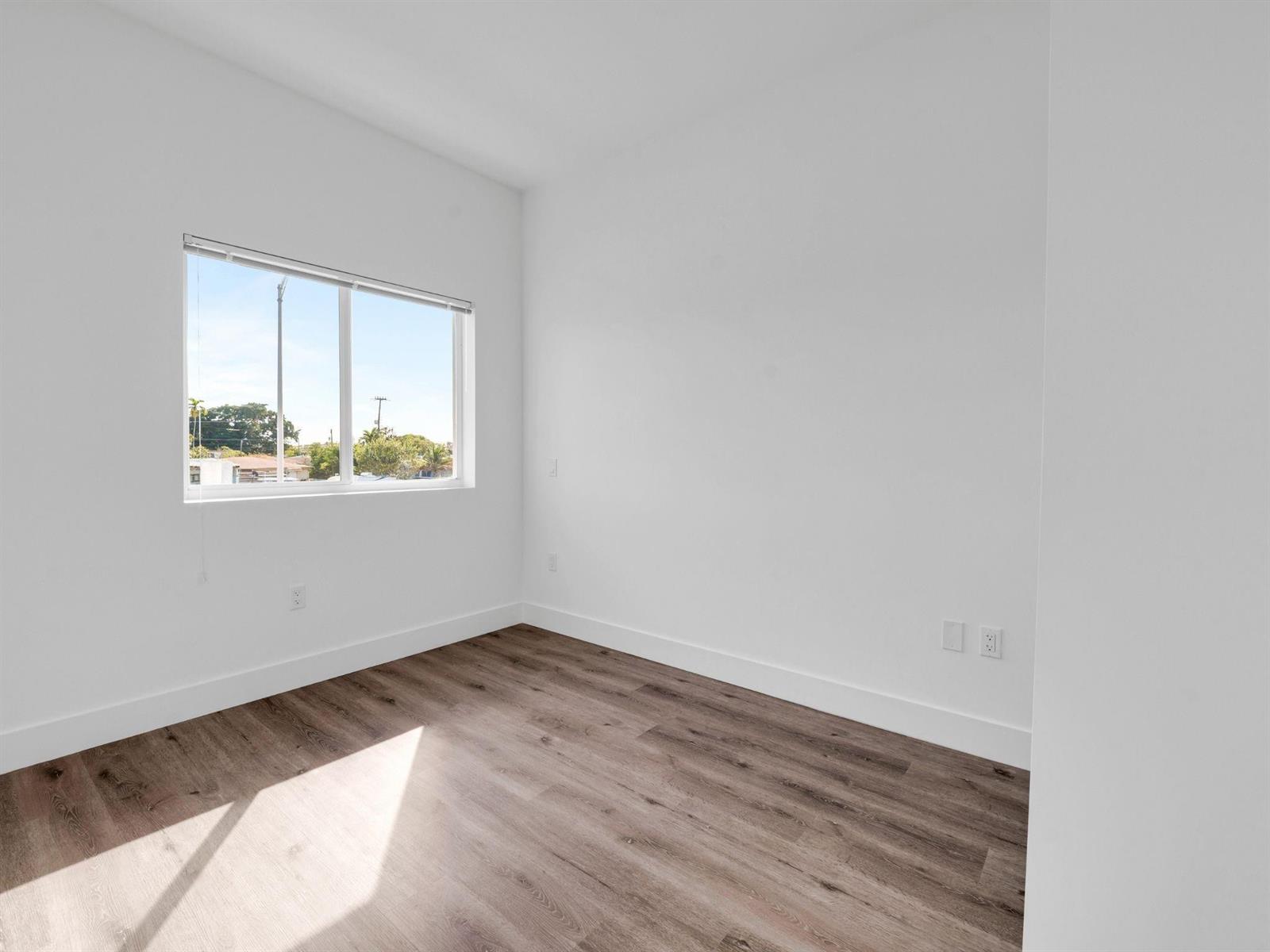 An empty room features white walls, wood-look flooring, and a window with blinds — 2130 NW 37th Street, Miami FL 33142, MIAMI, FL