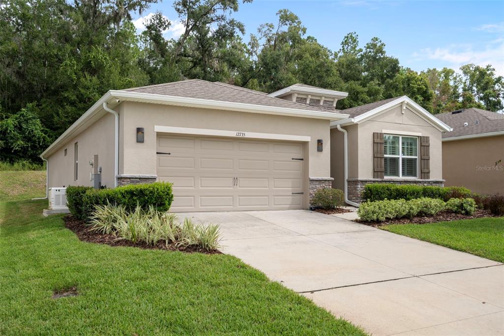A single-story house with a beige stucco exterior, a two-car garage, and a landscaped lawn — 12735 EASTPOINTE DRIVE, DADE CITY, FL