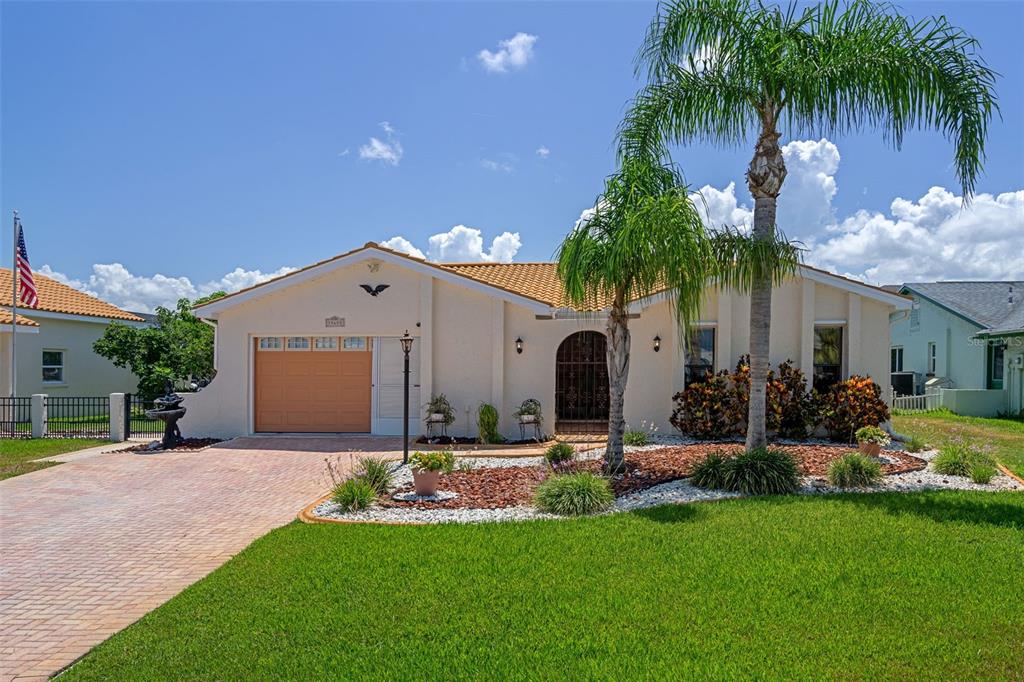 A single-story house with a tan stucco exterior, a tiled roof, and a palm tree — 15602 CENTURY DRIVE, HUDSON, FL