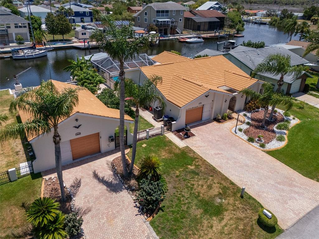 An aerial view shows a house with a detached garage, tiled roof, and waterfront access — 15602 CENTURY DRIVE, HUDSON, FL