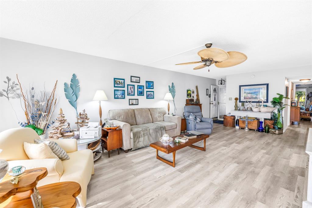 A living room features light wood-look flooring, a beige sofa, a blue armchair, and decor — 1655 S HIGHLAND AVENUE UNIT J187, CLEARWATER, FL