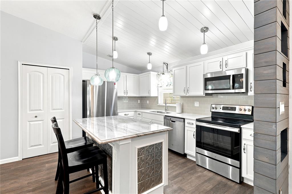A kitchen features white cabinets, a marble-topped island, stainless steel appliances, and wood-look flooring — 36 ROYAL PALM LANE, PALM COAST, FL