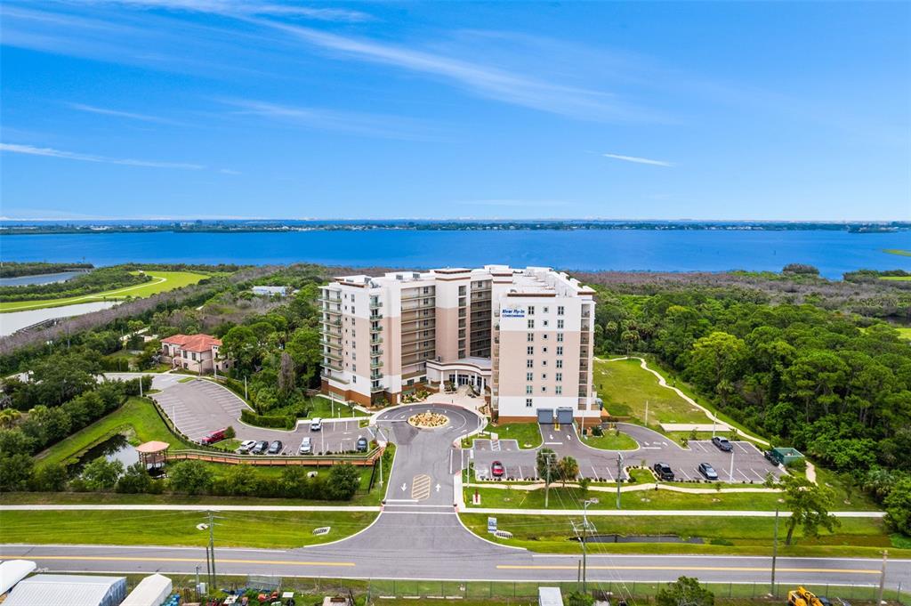 An aerial view shows a multi-story condominium building surrounded by parking lots, trees, and water — 735 W PILOT LANE UNIT 506, MERRITT ISLAND, FL