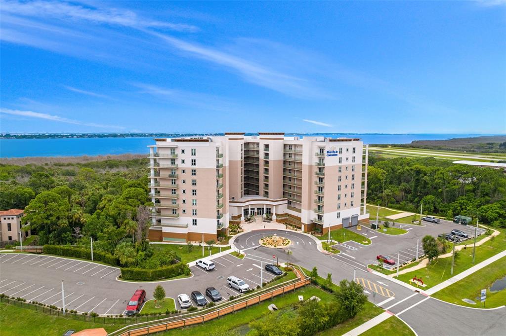 An aerial view shows a multi-story condominium building surrounded by trees, parking lots, and water — 735 W PILOT LANE UNIT 506, MERRITT ISLAND, FL