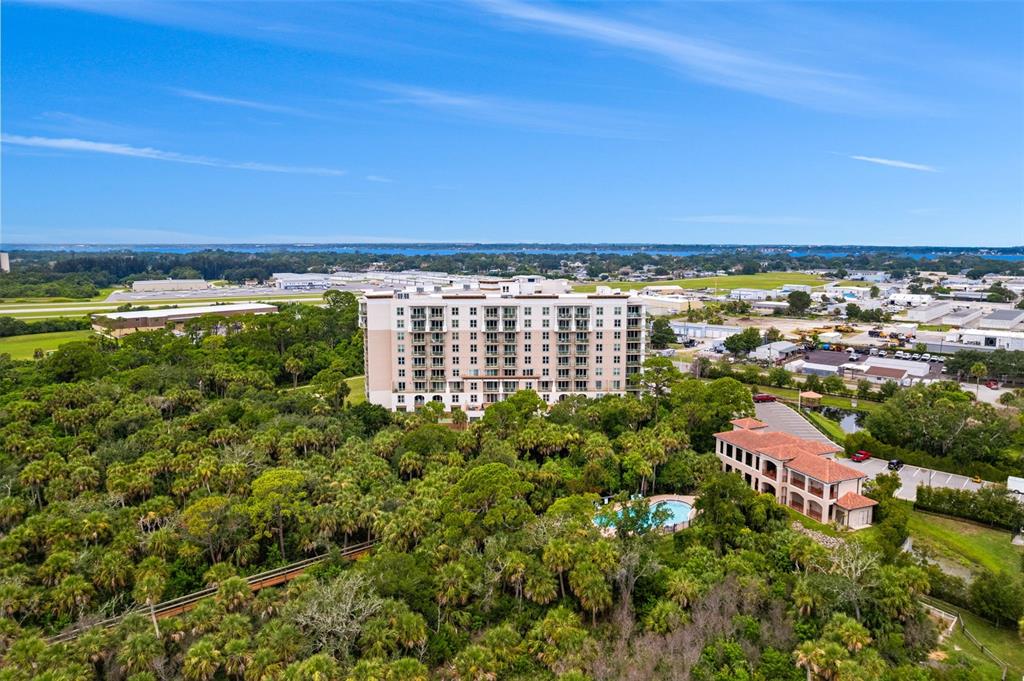 An aerial view shows a multi-story apartment building surrounded by dense trees and a pool — 735 W PILOT LANE UNIT 506, MERRITT ISLAND, FL