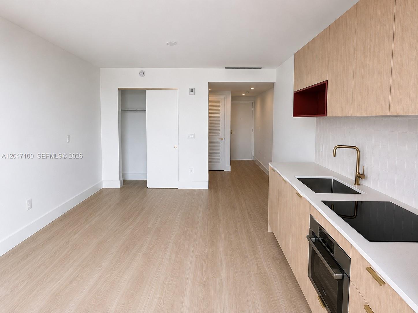 A modern studio apartment features light wood flooring, white walls, and a compact kitchen area — 90 NE 32nd St # 1126, Miami FL 33127, MIAMI, FL